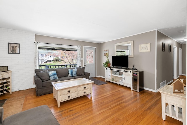 living area with wine cooler, light wood-type flooring, visible vents, baseboards, and ornamental molding