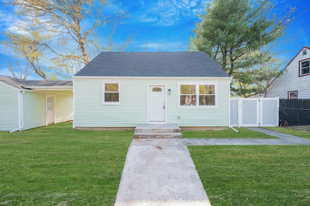 view of front of home with fence, roof with shingles, a gate, and a front lawn