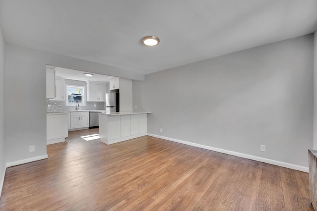 unfurnished living room featuring a sink, light wood finished floors, and baseboards