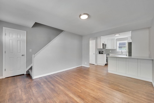 unfurnished living room featuring light wood finished floors, stairs, and baseboards