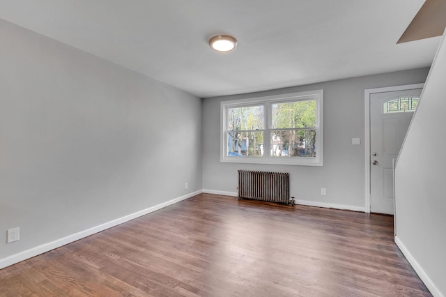unfurnished living room with wood finished floors, baseboards, and radiator