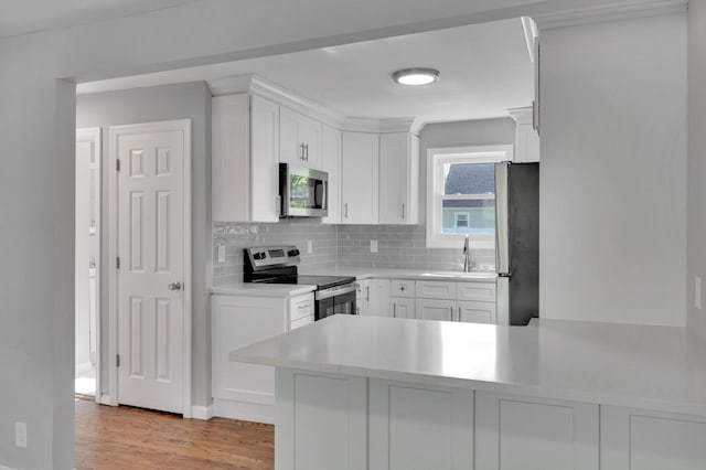 kitchen with a sink, light wood-style floors, tasteful backsplash, white cabinets, and appliances with stainless steel finishes