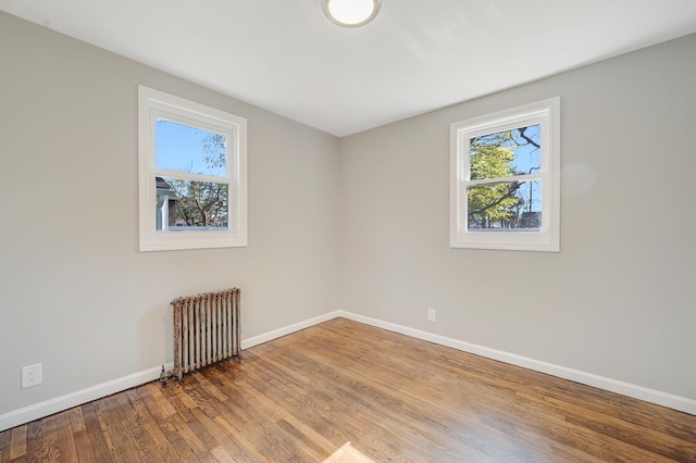 unfurnished room featuring baseboards, radiator heating unit, and wood finished floors