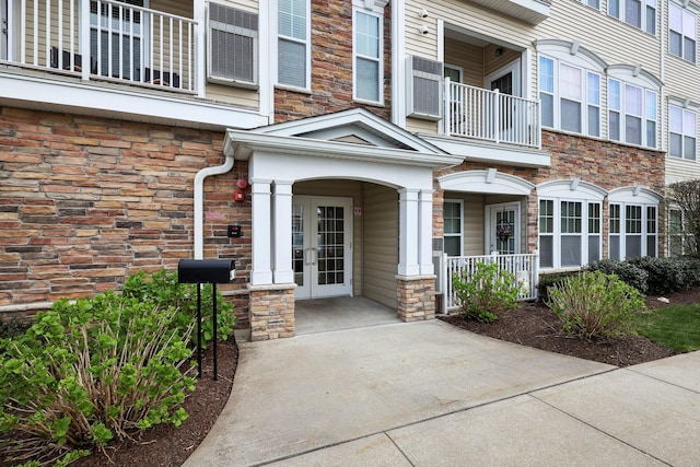 view of exterior entry featuring french doors, a porch, a balcony, and stone siding