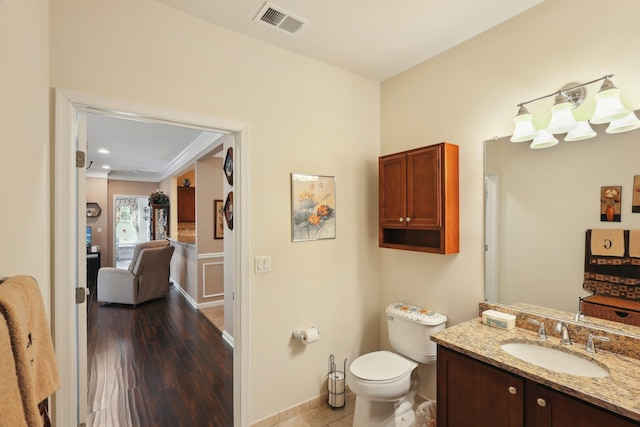 half bath with vanity, toilet, visible vents, baseboards, and wood finished floors