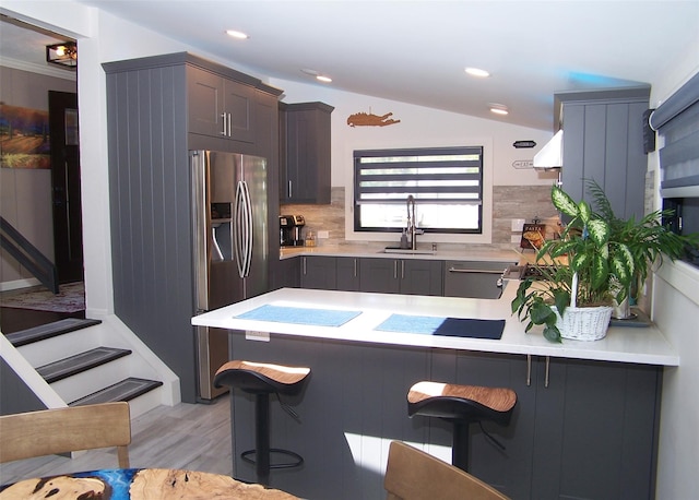 kitchen featuring stainless steel refrigerator with ice dispenser, a sink, a breakfast bar, and tasteful backsplash