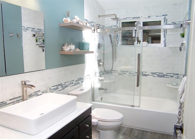 bathroom with vanity, toilet, combined bath / shower with glass door, wood finished floors, and tasteful backsplash