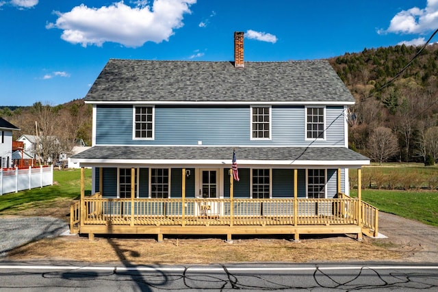 farmhouse inspired home with covered porch, a front lawn, a chimney, and a shingled roof