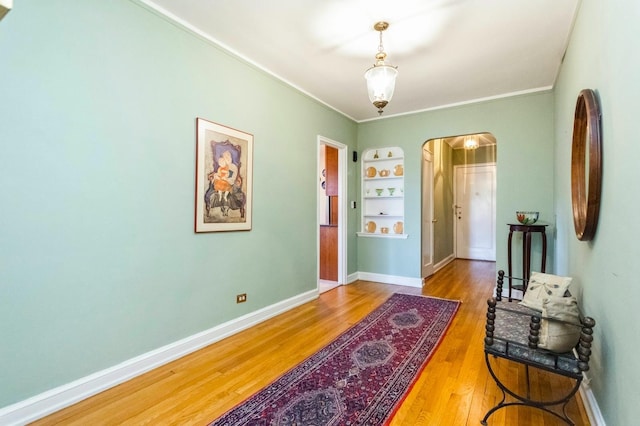 foyer entrance featuring arched walkways, baseboards, ornamental molding, and wood finished floors