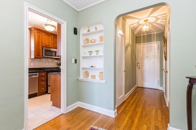 hall with arched walkways, baseboards, built in shelves, and light wood finished floors