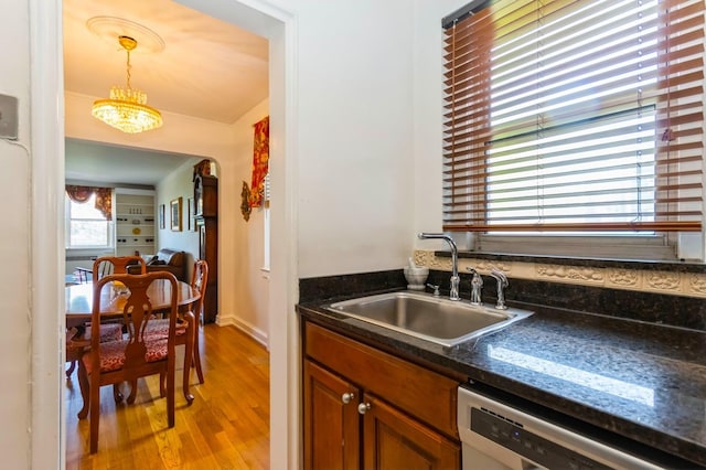 kitchen with brown cabinetry, light wood-style floors, dishwashing machine, a sink, and hanging light fixtures