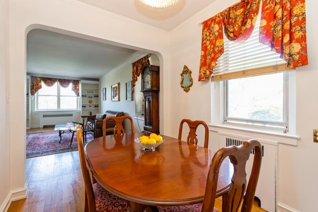 dining room with arched walkways, wood finished floors, baseboards, radiator, and ornamental molding