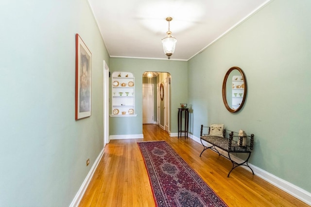 hallway with arched walkways, ornamental molding, baseboards, and light wood-style flooring