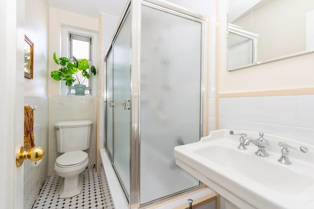 bathroom featuring toilet, tile walls, a sink, and a stall shower