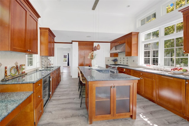 kitchen featuring high end stove, a sink, wine cooler, under cabinet range hood, and light wood-style flooring