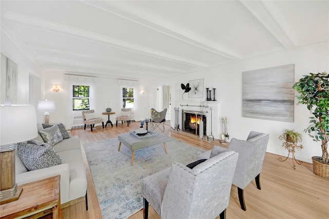 living area with beamed ceiling, light wood finished floors, and a warm lit fireplace