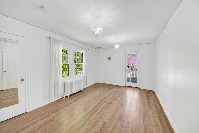 spare room with wood finished floors, baseboards, radiator heating unit, and a chandelier