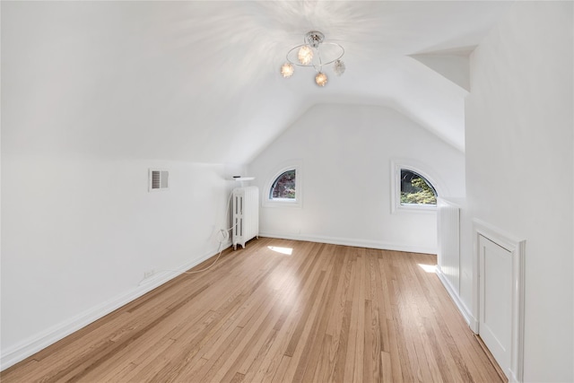 bonus room featuring a notable chandelier, radiator heating unit, vaulted ceiling, light wood-type flooring, and visible vents