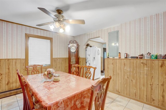 dining space featuring wainscoting, wooden walls, light tile patterned floors, a ceiling fan, and arched walkways