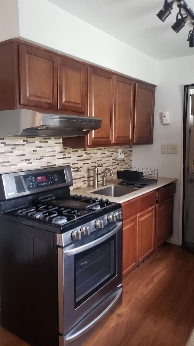 2261 Story Ave, Bronx, NY 10473 - kitchen featuring stainless steel gas stove, under cabinet range hood, wood finished floors, tasteful backsplash, and brown cabinetry