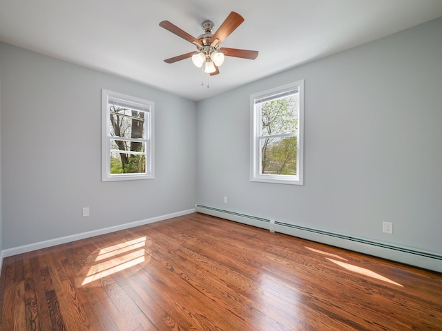 spare room featuring baseboard heating, baseboards, wood finished floors, and a ceiling fan