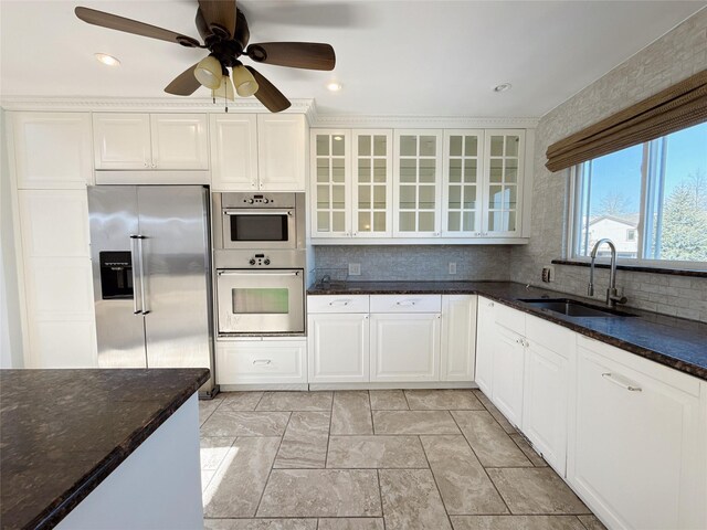 kitchen featuring dark stone counters, a sink, stainless steel appliances, decorative backsplash, and glass insert cabinets
