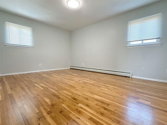 empty room with baseboards, a baseboard heating unit, and light wood finished floors