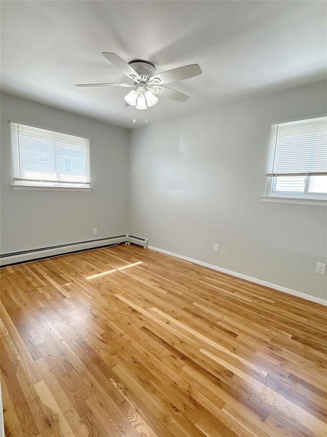 empty room featuring ceiling fan, a healthy amount of sunlight, light wood-type flooring, and a baseboard heating unit