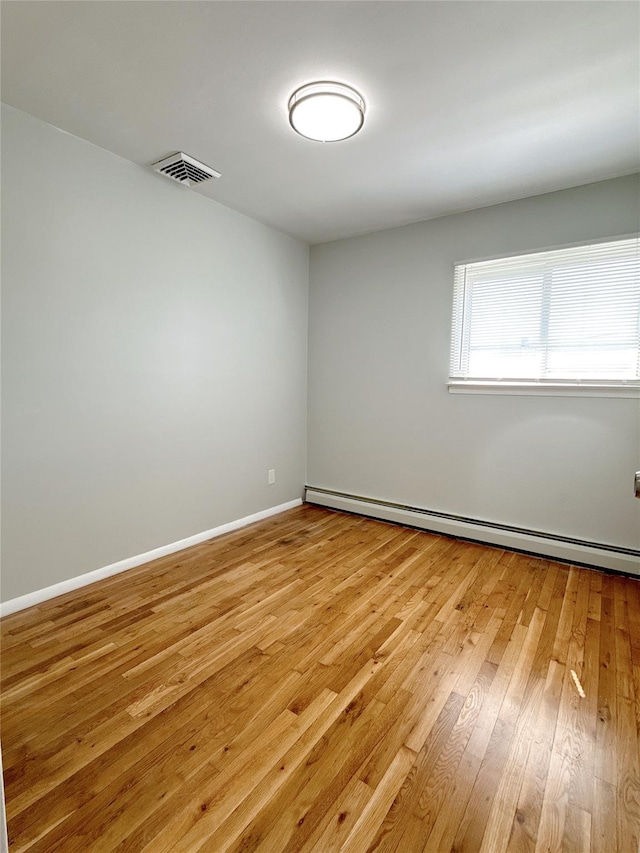 spare room with baseboards, visible vents, light wood-type flooring, and a baseboard radiator