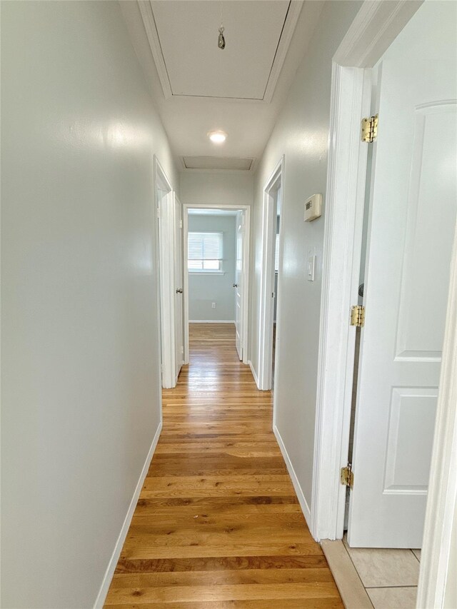 hall featuring baseboards, attic access, and light wood-style flooring
