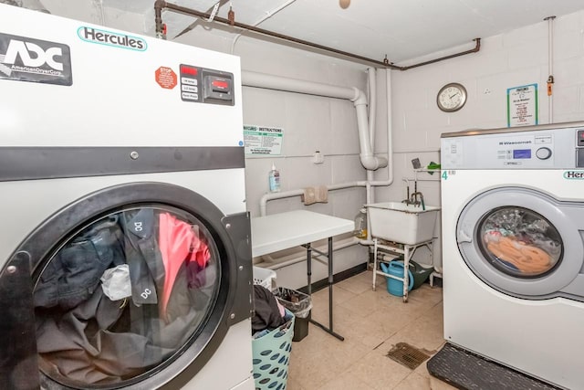 shared laundry area featuring concrete block wall, washer and clothes dryer, and a sink
