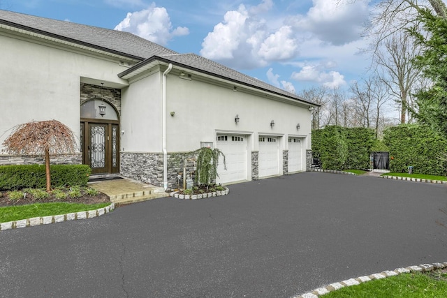 view of home's exterior featuring an attached garage, driveway, stone siding, and stucco siding