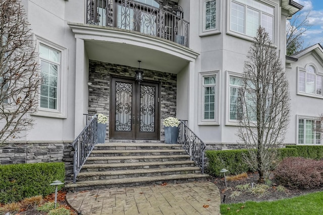 entrance to property with stucco siding, a balcony, and stone siding