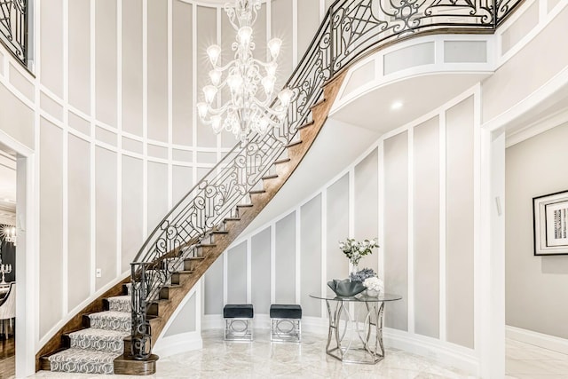 staircase with a high ceiling, a chandelier, marble finish floor, a decorative wall, and baseboards