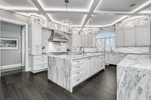 kitchen with a sink, a chandelier, coffered ceiling, under cabinet range hood, and light stone countertops