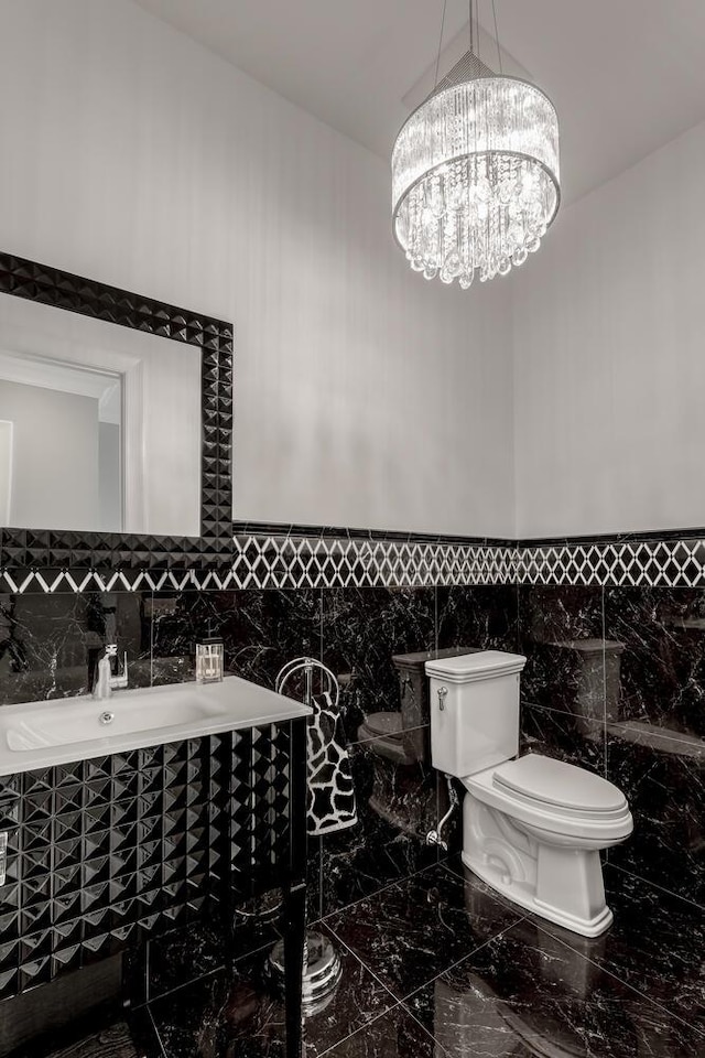 bathroom with tile walls, an inviting chandelier, toilet, and marble finish floor