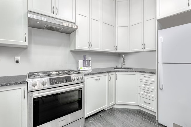 kitchen with freestanding refrigerator, under cabinet range hood, white cabinets, a sink, and stainless steel range with gas stovetop
