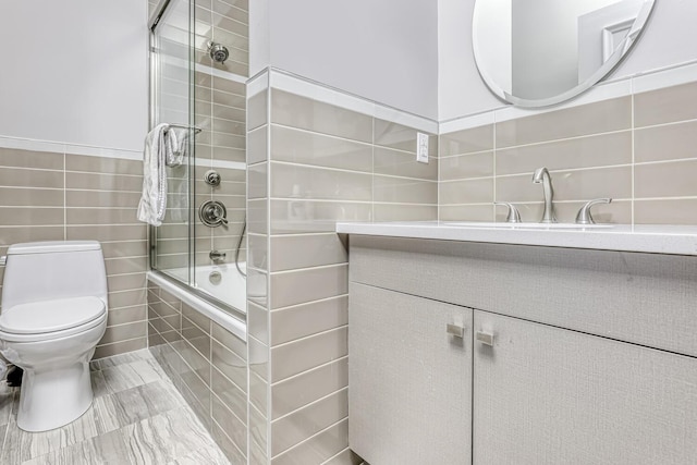 bathroom featuring toilet, vanity, tiled shower / bath, and tile walls