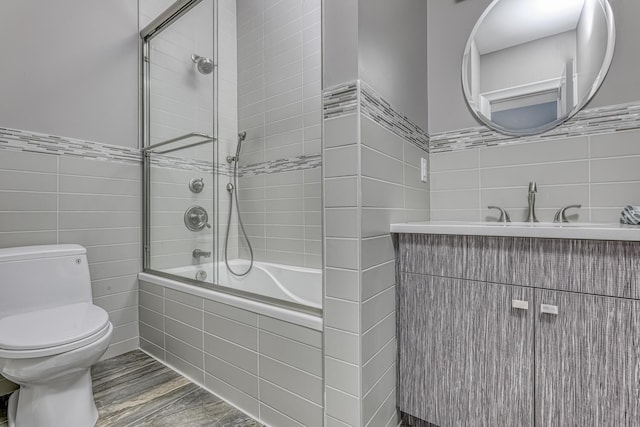 full bathroom featuring tiled shower / bath combo, toilet, tile walls, wood finished floors, and vanity