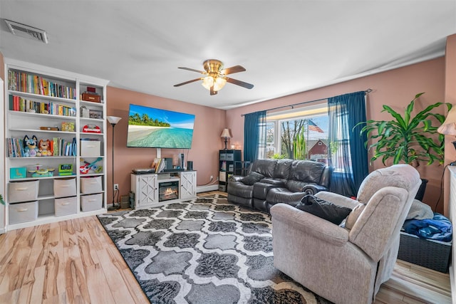 living room with wood finished floors, visible vents, ceiling fan, and baseboards