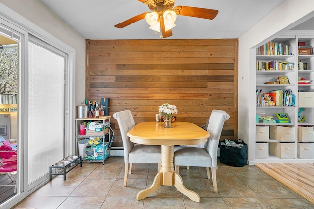 dining room featuring wooden walls, light tile patterned flooring, ceiling fan, and a baseboard radiator