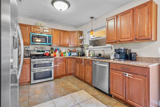 kitchen featuring light stone countertops, a sink, brown cabinetry, pendant lighting, and appliances with stainless steel finishes