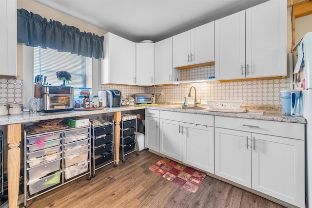kitchen featuring light wood-style flooring, decorative backsplash, a toaster, white cabinets, and a sink