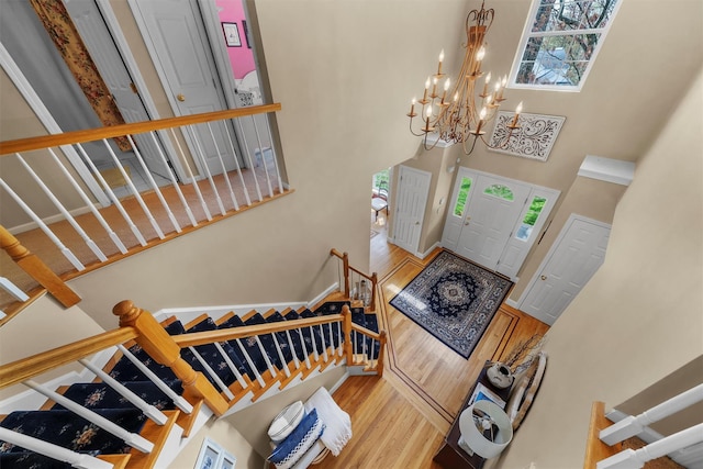 entryway featuring a towering ceiling, wood finished floors, a chandelier, and stairway