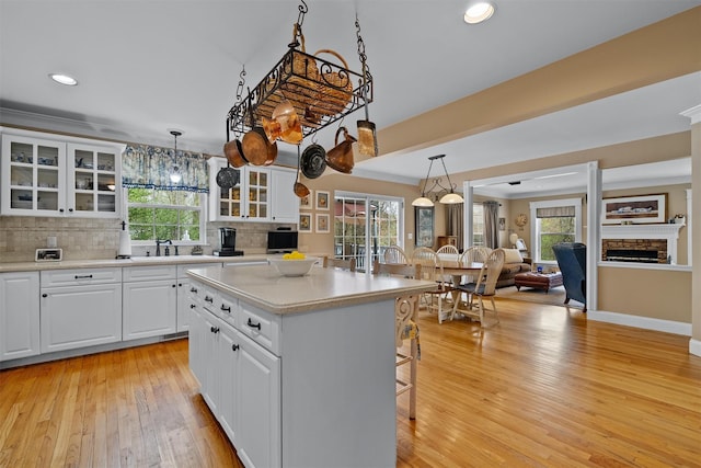 kitchen with hanging light fixtures, glass insert cabinets, light wood-style flooring, and a kitchen bar