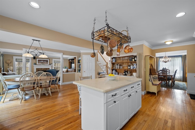 kitchen featuring an inviting chandelier, a fireplace, light countertops, white cabinets, and light wood-style flooring