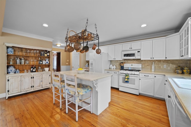 kitchen featuring a breakfast bar area, crown molding, light countertops, white cabinets, and white appliances