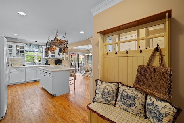 kitchen with a kitchen breakfast bar, light wood finished floors, glass insert cabinets, white fridge with ice dispenser, and white cabinetry