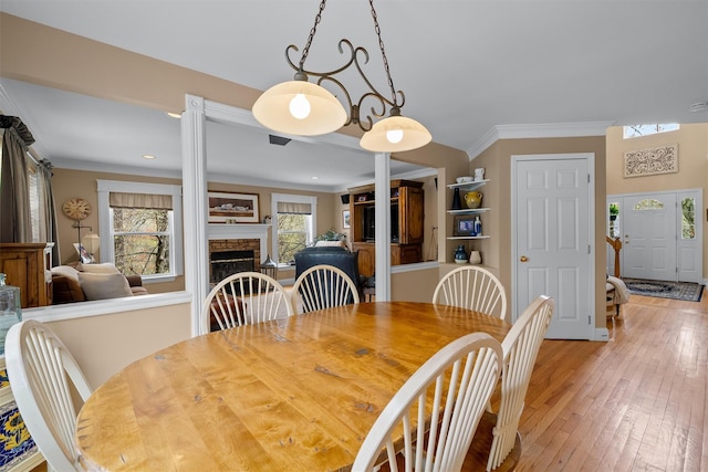 dining space featuring light wood-style floors, ornamental molding, and a stone fireplace