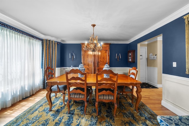 dining room featuring an inviting chandelier, ornamental molding, wainscoting, and light wood finished floors